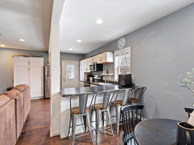 kitchen with stainless steel appliances, a sink, white cabinets, a kitchen breakfast bar, and dark wood finished floors