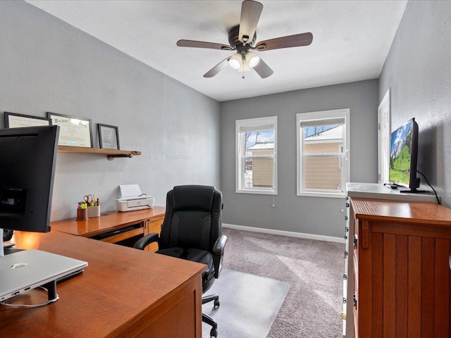 carpeted office space featuring a ceiling fan and baseboards