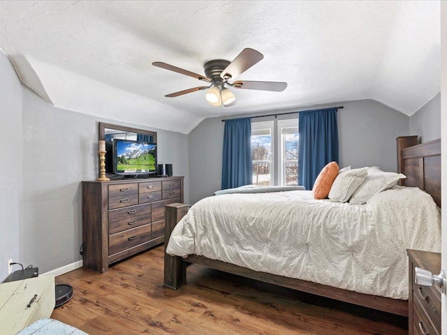 bedroom with ceiling fan, vaulted ceiling, a textured ceiling, wood finished floors, and baseboards