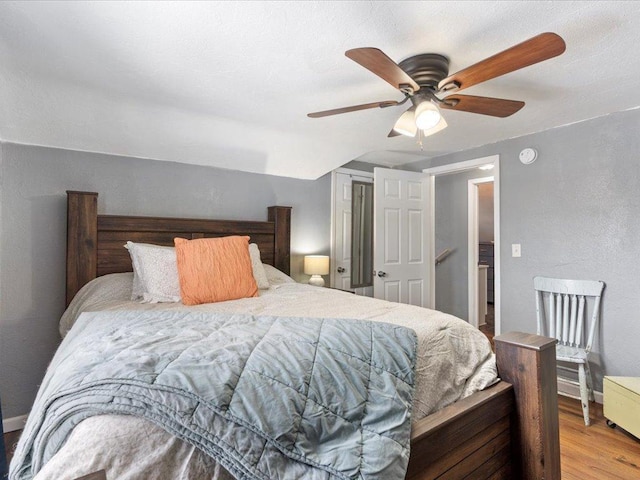 bedroom with a ceiling fan, a textured wall, baseboards, and wood finished floors