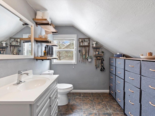 bathroom with a textured ceiling, toilet, vanity, baseboards, and vaulted ceiling