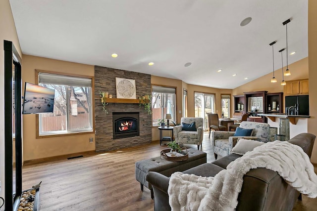 living room with visible vents, light wood-style floors, a fireplace, baseboards, and vaulted ceiling