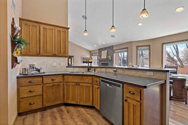 kitchen featuring a peninsula, a sink, dishwasher, dark countertops, and brown cabinets