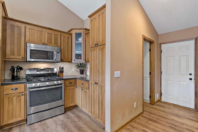 kitchen with dark countertops, tasteful backsplash, stainless steel appliances, light wood finished floors, and lofted ceiling