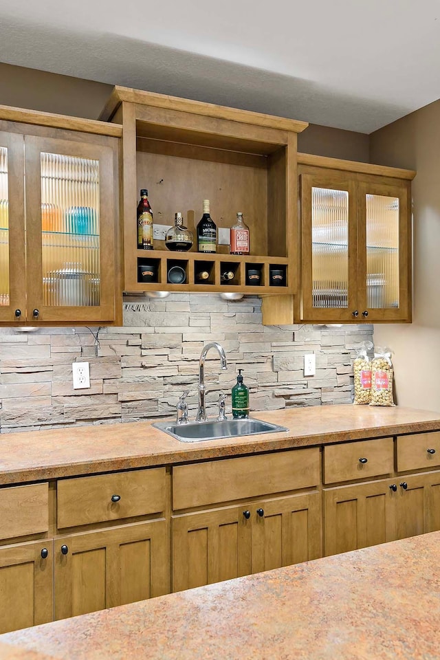 kitchen featuring light countertops, glass insert cabinets, tasteful backsplash, and a sink