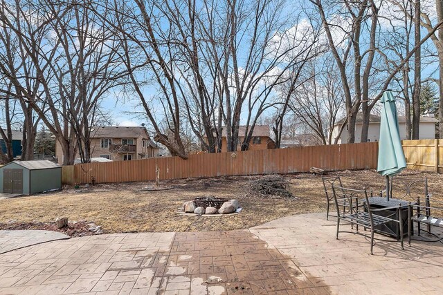 view of patio with a storage shed, a fenced backyard, an outbuilding, and a fire pit