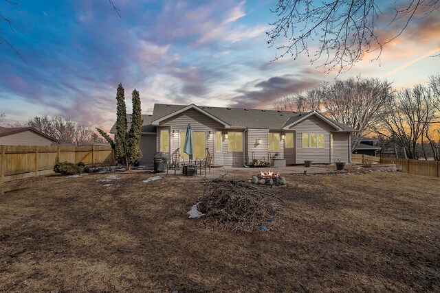 back of property at dusk featuring a patio area, a lawn, an outdoor fire pit, and a fenced backyard