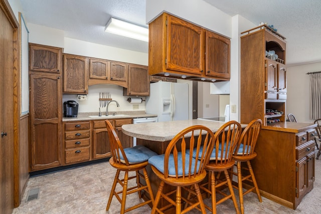 kitchen featuring visible vents, a peninsula, light countertops, white fridge with ice dispenser, and a sink