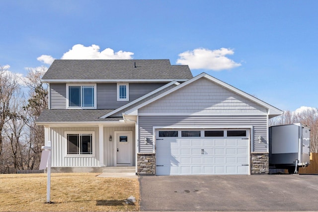 view of front of property with a shingled roof, a garage, stone siding, driveway, and a front lawn