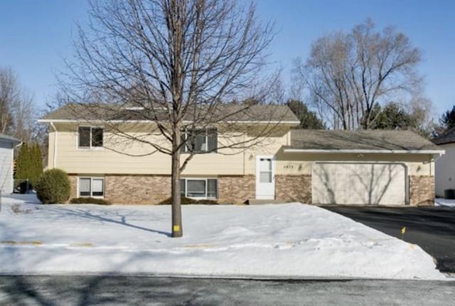 view of front of property featuring a garage, central air condition unit, brick siding, and aphalt driveway