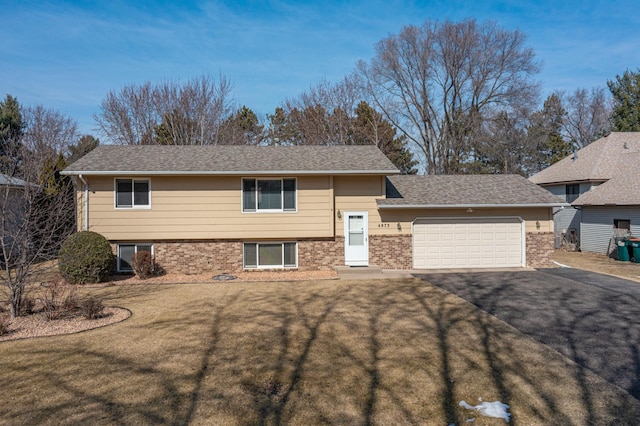 tri-level home featuring a front yard, a garage, brick siding, and aphalt driveway