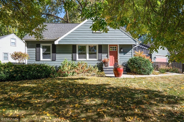 view of front of house with a shingled roof, a front yard, and fence