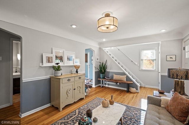 living room with light wood-style floors, arched walkways, stairway, and baseboards