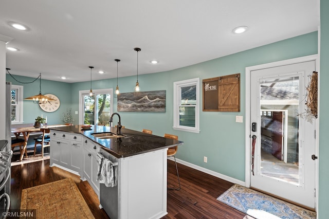 kitchen featuring a kitchen island with sink, dark wood-type flooring, a sink, stainless steel dishwasher, and dark countertops