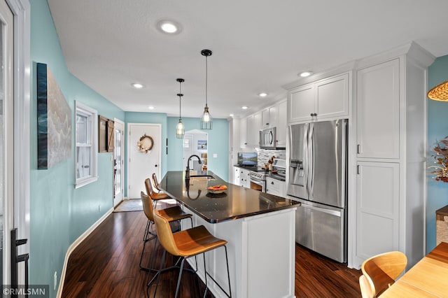 kitchen featuring dark countertops, appliances with stainless steel finishes, white cabinetry, a sink, and an island with sink