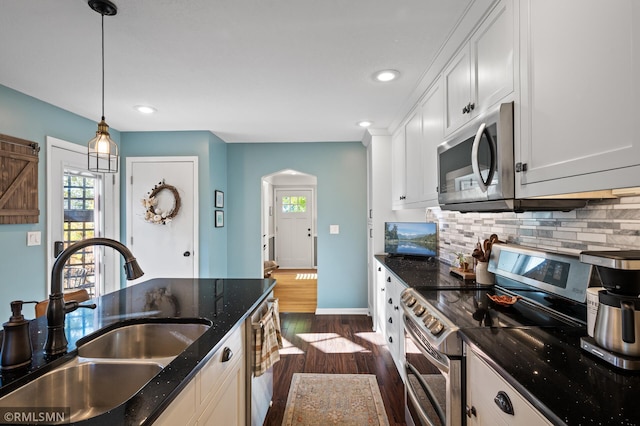 kitchen featuring arched walkways, decorative backsplash, dark wood-style floors, stainless steel appliances, and a sink