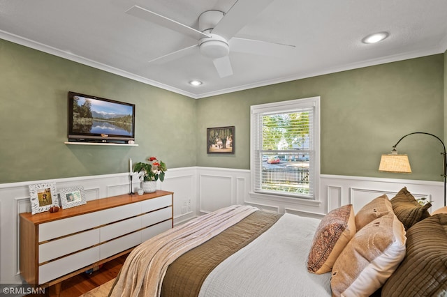 bedroom featuring ceiling fan, wainscoting, wood finished floors, and crown molding