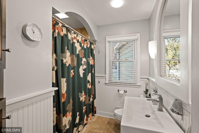 full bathroom featuring toilet, a wainscoted wall, curtained shower, and a sink