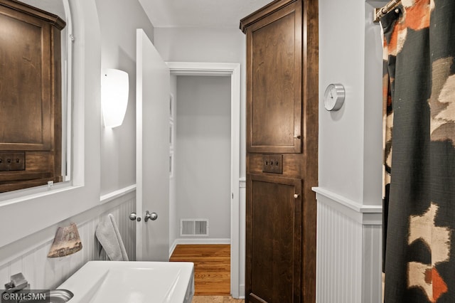 bathroom with a wainscoted wall, wood finished floors, visible vents, and a decorative wall