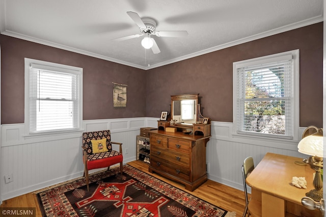 living area with a wainscoted wall, crown molding, a ceiling fan, and wood finished floors