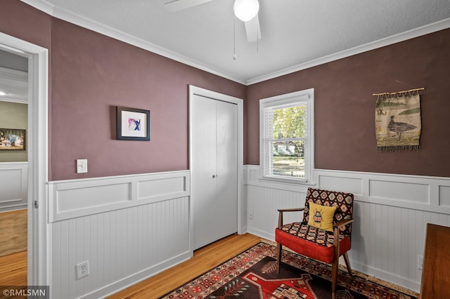 living area with a ceiling fan, wainscoting, ornamental molding, and wood finished floors