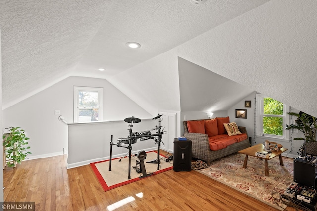 exercise area with lofted ceiling, hardwood / wood-style flooring, baseboards, and a textured ceiling