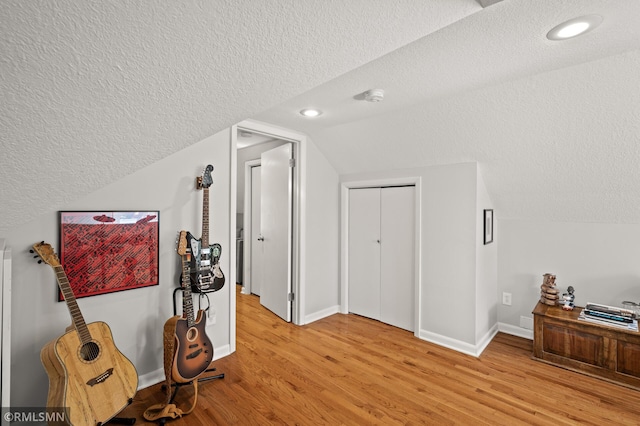 corridor featuring light wood-style floors, vaulted ceiling, a textured ceiling, and baseboards