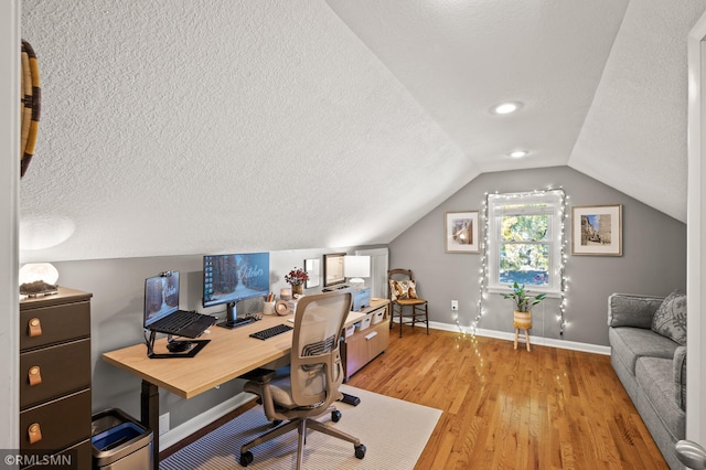 office featuring lofted ceiling, light wood-style flooring, baseboards, and a textured ceiling