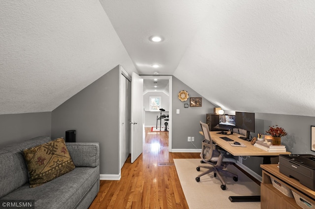 office area featuring light wood-style floors, baseboards, vaulted ceiling, and a textured ceiling