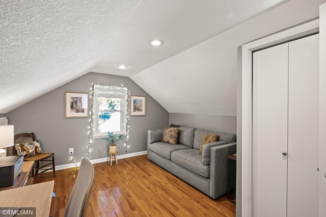 living area with lofted ceiling, wood-type flooring, baseboards, and a textured ceiling