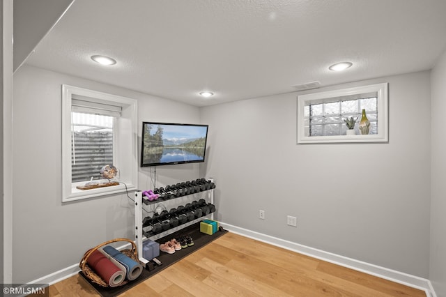 exercise room featuring a textured ceiling, baseboards, and wood finished floors