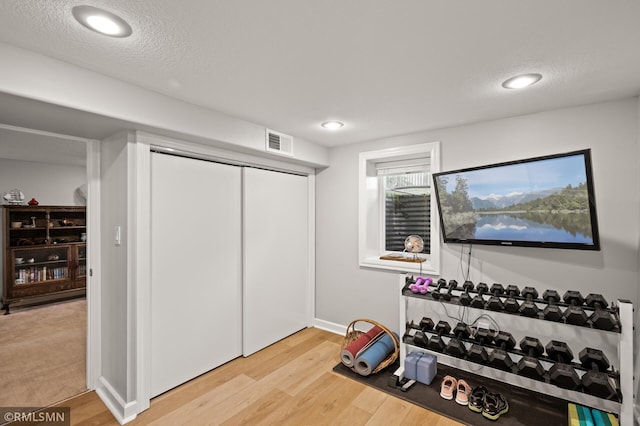 workout room featuring baseboards, visible vents, a textured ceiling, and light wood finished floors