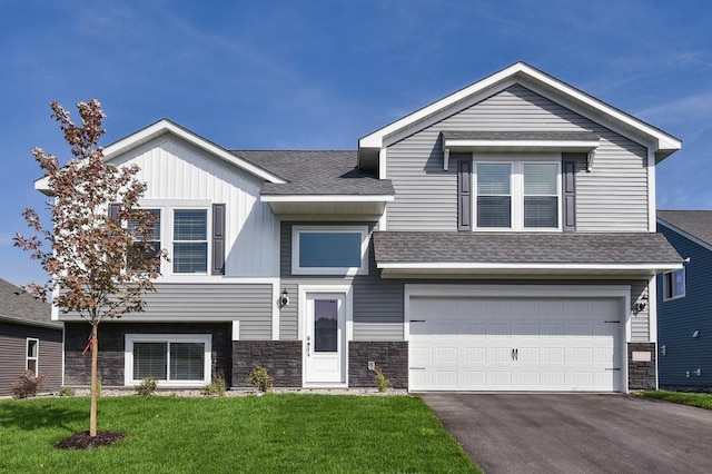 view of front of property with an attached garage, driveway, stone siding, roof with shingles, and a front yard