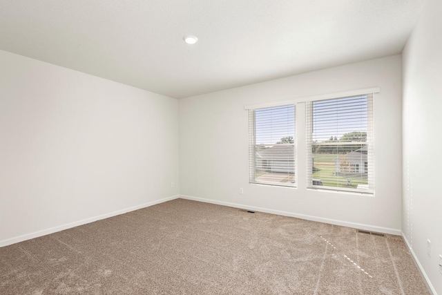 unfurnished room with carpet, visible vents, and baseboards