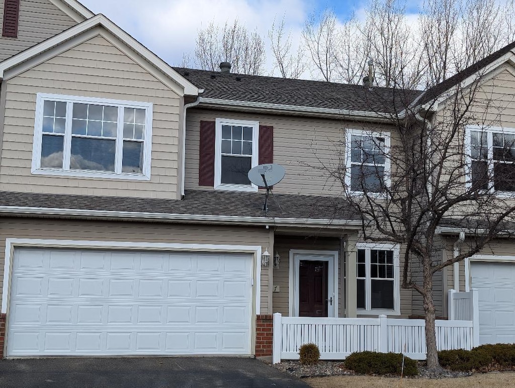 multi unit property with a garage, a shingled roof, and driveway