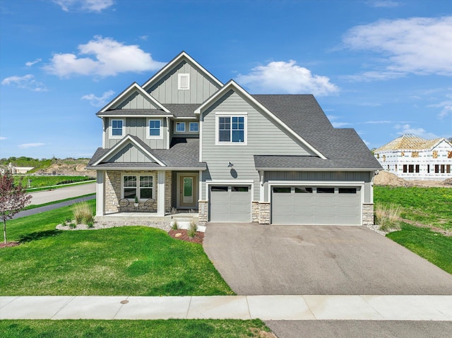 craftsman-style house featuring stone siding, roof with shingles, an attached garage, a front lawn, and board and batten siding