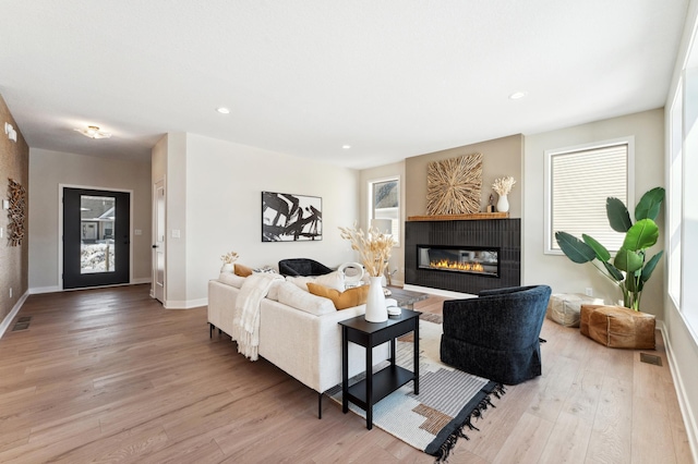 living area featuring light wood-type flooring, visible vents, a glass covered fireplace, recessed lighting, and baseboards