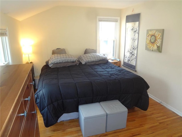 bedroom with light wood finished floors, baseboards, and vaulted ceiling