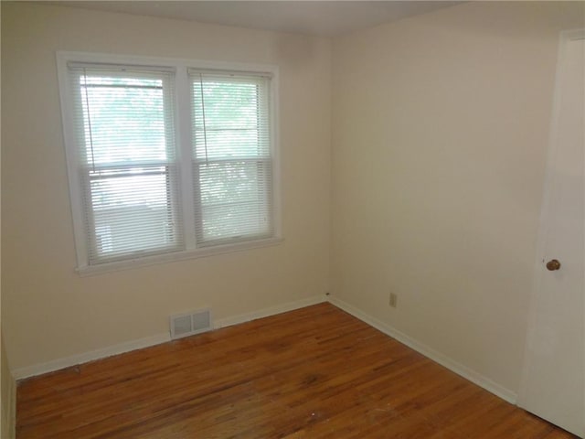 unfurnished room featuring wood finished floors, visible vents, and baseboards