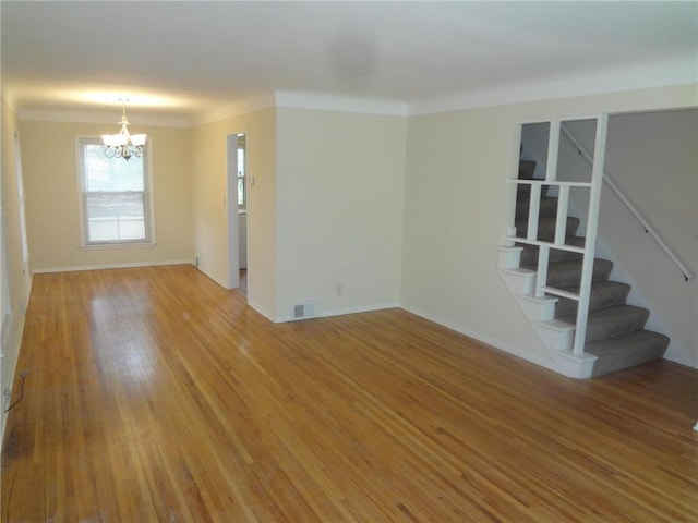 empty room with crown molding, visible vents, light wood-style flooring, stairway, and an inviting chandelier