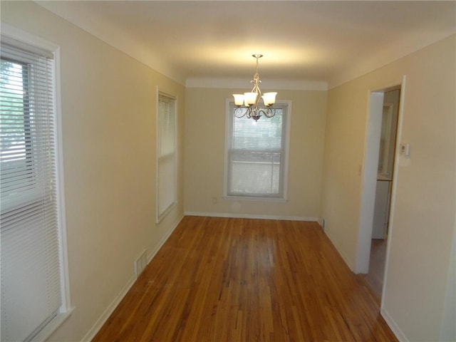 unfurnished dining area featuring baseboards, a chandelier, a wealth of natural light, and wood finished floors