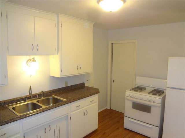 kitchen featuring dark countertops, white appliances, white cabinets, and a sink