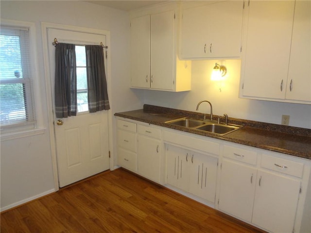 kitchen with dark countertops, a sink, dark wood finished floors, and white cabinetry