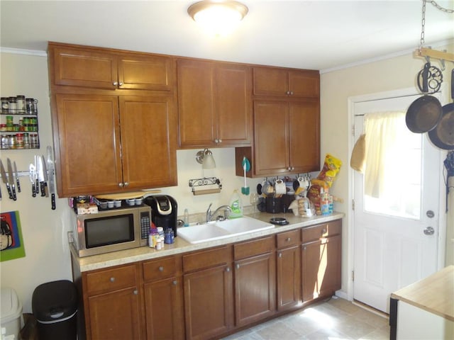 kitchen with a sink, light countertops, ornamental molding, brown cabinets, and stainless steel microwave