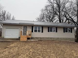 ranch-style home featuring a garage, dirt driveway, and metal roof