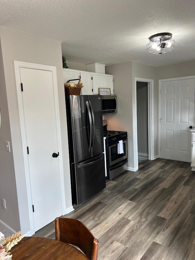 kitchen featuring stainless steel appliances, white cabinets, a textured ceiling, wood finished floors, and baseboards