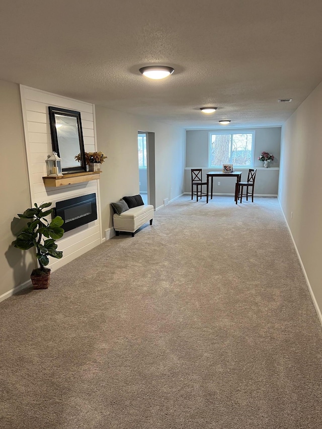 living area with a textured ceiling, carpet floors, a glass covered fireplace, and baseboards