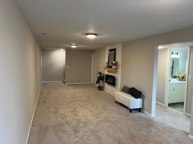 living area with a textured ceiling, carpet flooring, a glass covered fireplace, and baseboards