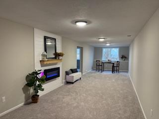 living area featuring baseboards, carpet flooring, and a glass covered fireplace