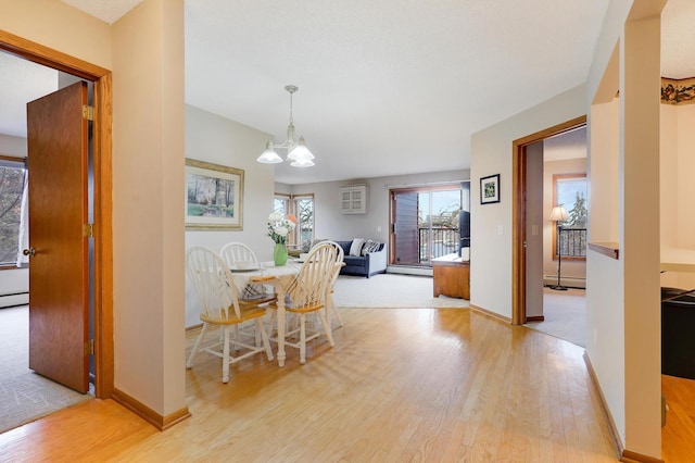 dining room with a notable chandelier, a baseboard heating unit, an AC wall unit, light wood-type flooring, and baseboards